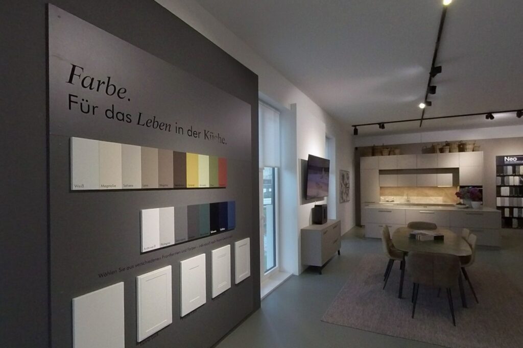 Farbwand mit Frontmustern in der Ausstellung von Neo, dahinter Esstisch und eine helle Musterküche