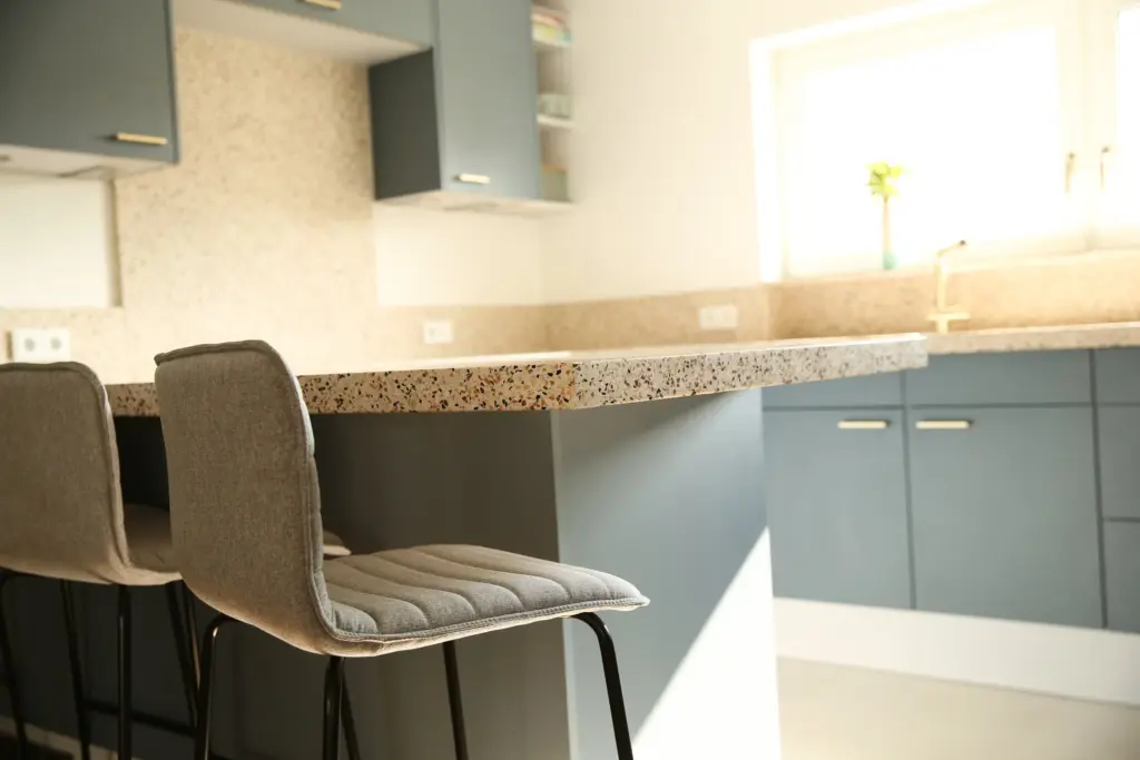 Küchentheke mit Terrazzo-Arbeitsplatte und grau-blauen Fronten, davor zwei Barhocker