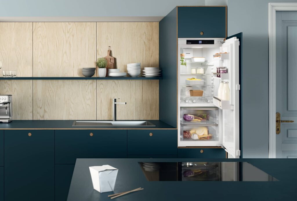Geöffnetes Liebherr Einbaugerät der Plus-Serie in einer Küche mit petrolfarbenen Fronten und Holzrückwand