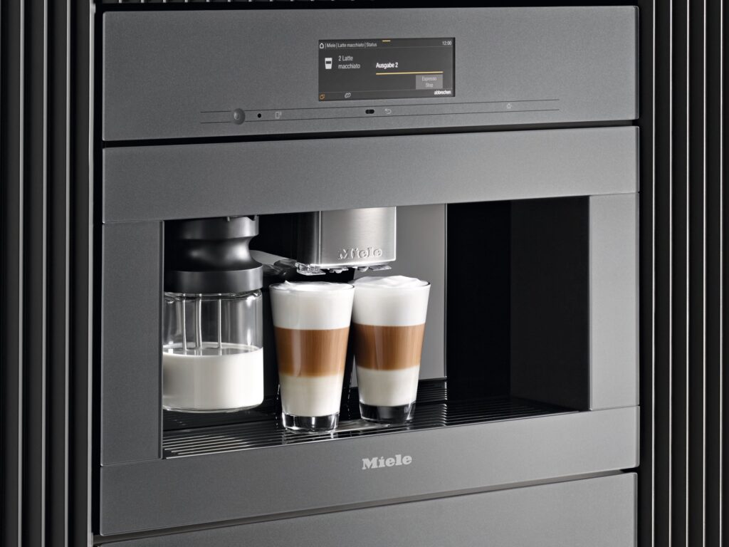 Miele Einbau-Kaffeevollautomat in grauer Front mit Milchbehälter und zwei Gläsern Latte Macchiato