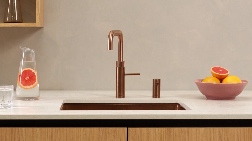 Quooker Fusion Square in Kupfer Rosé mit Seifenspender, daneben Karaffe mit Grapefruit